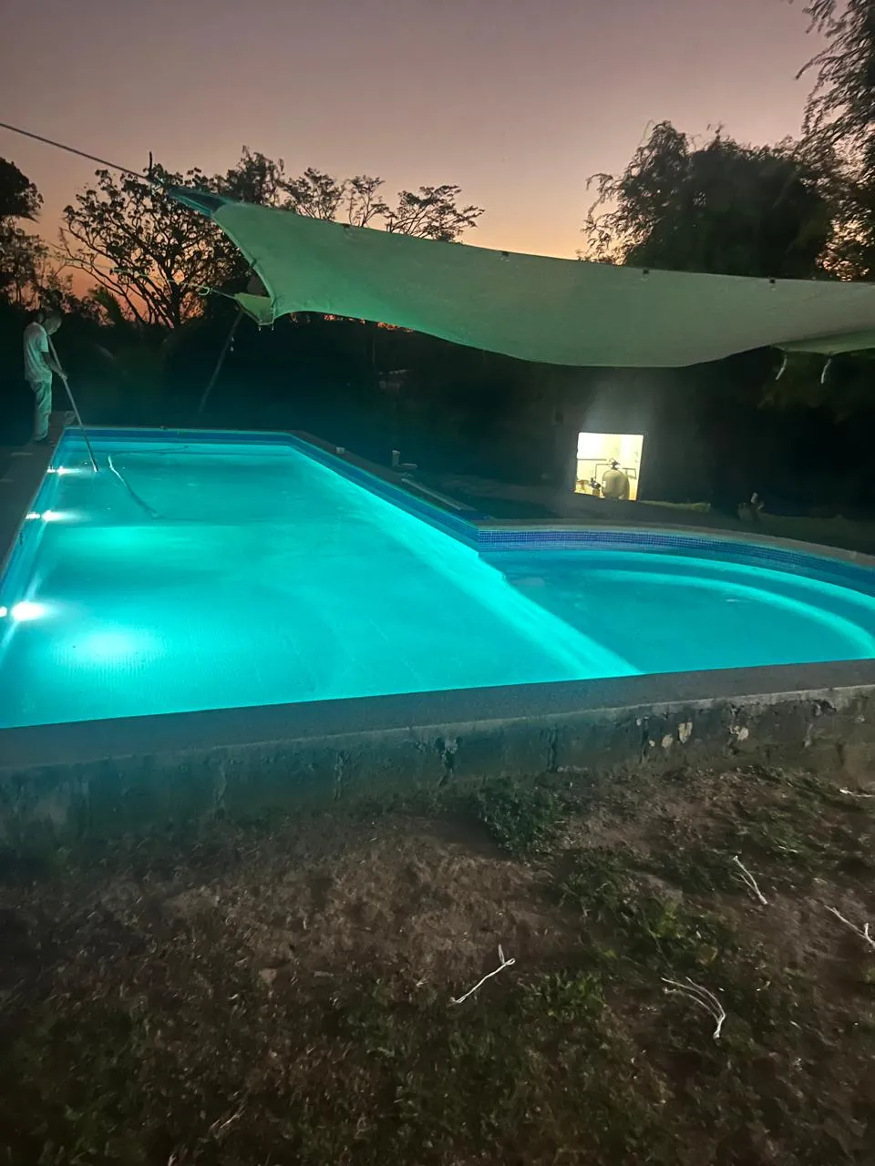 Alberca turquesa iluminada de noche con vela de sombra