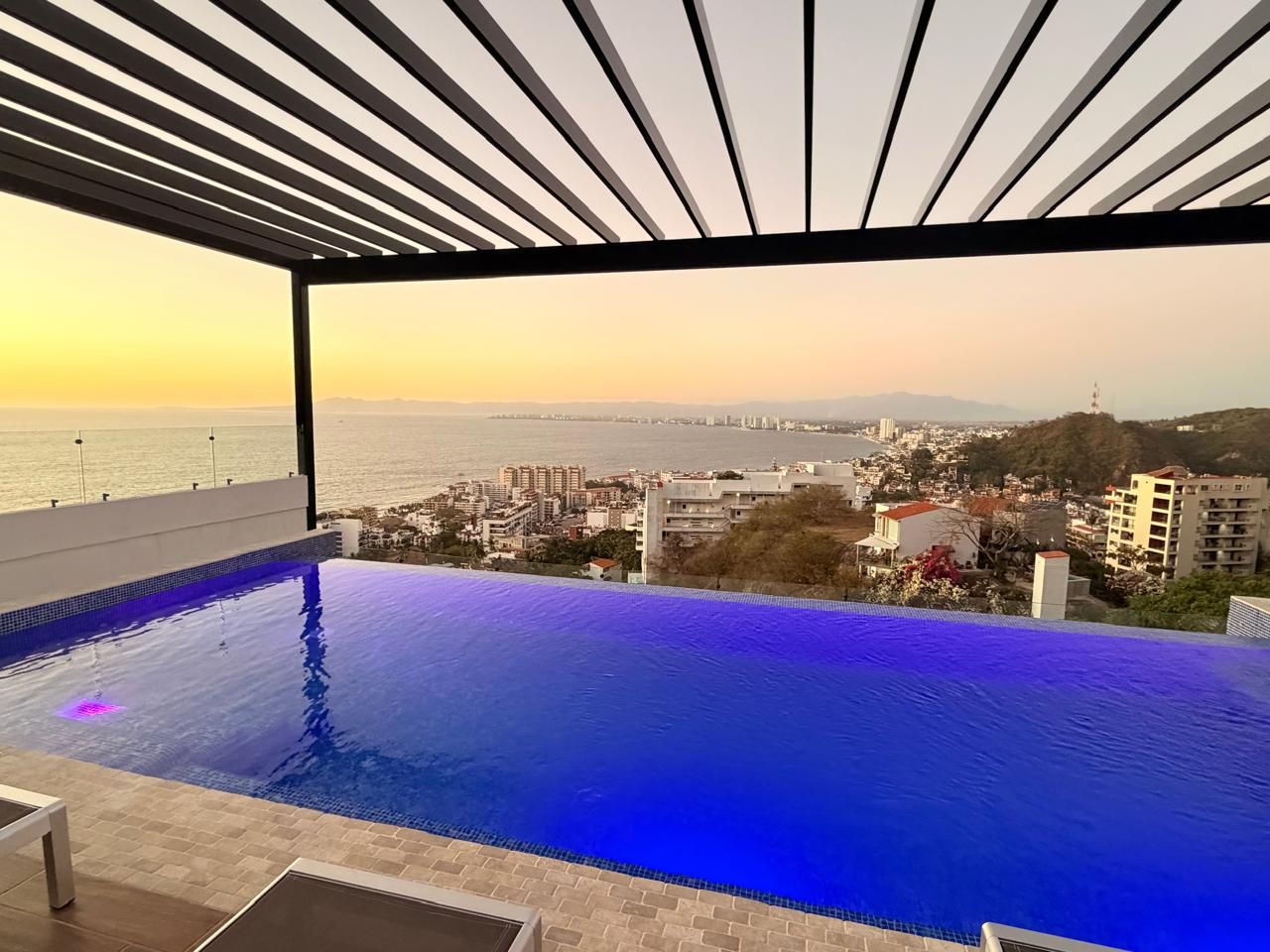 Alberca infinita bajo pérgola de acero al atardecer, con vista a la Bahía de Banderas