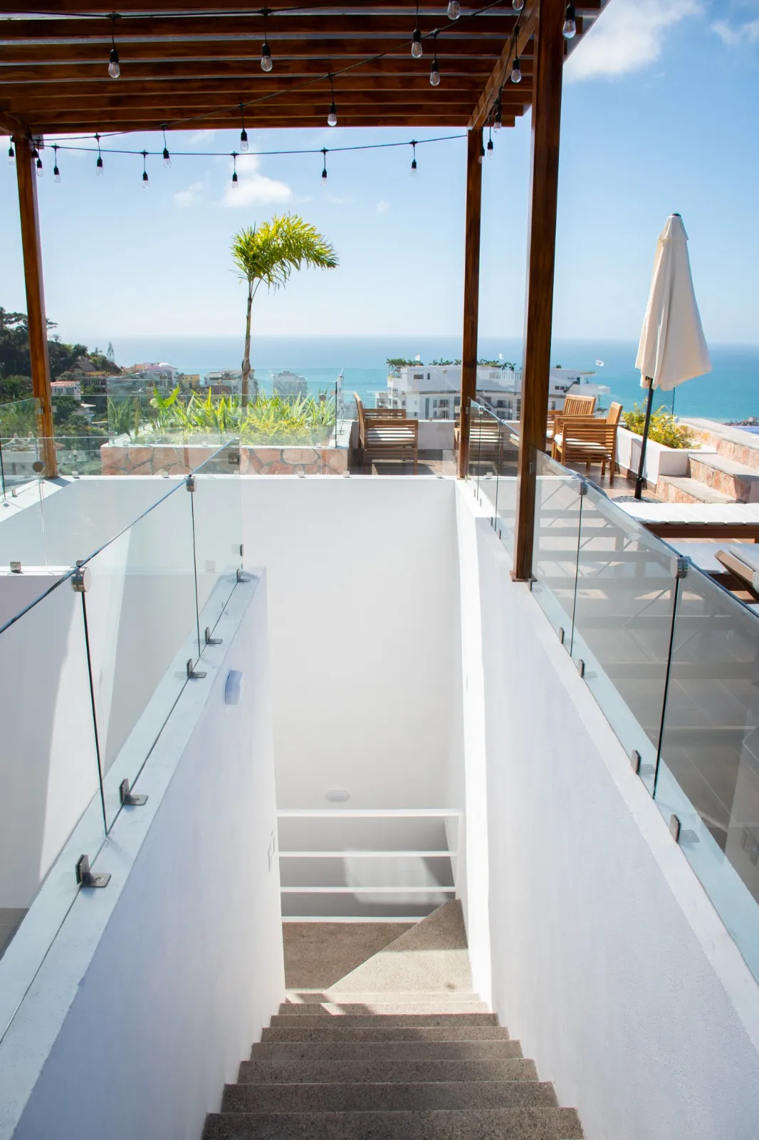 Roof garden con pérgola de madera, barandal de vidrio y vista al mar